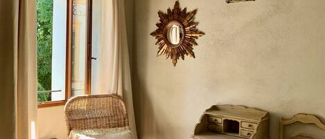 Une pièce comprenant une chaise en osier, une petite table, un lit et une fenêtre avec des rideaux.