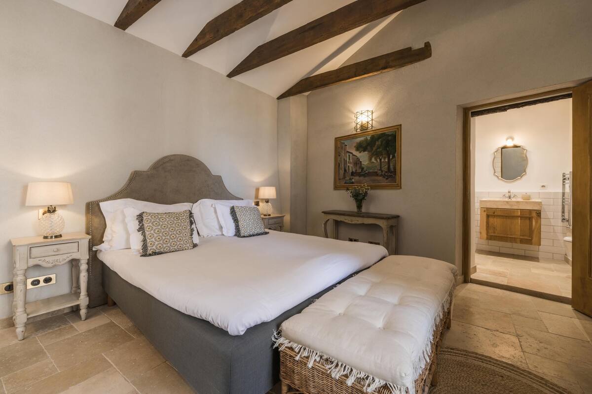 A bedroom with a large bed, two bedside tables with lamps, a painting on the wall, and a view into the bathroom.