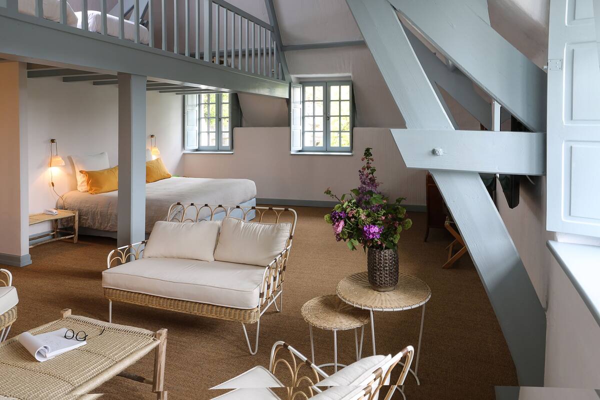 A cozy bedroom with a bed, a sofa, a small table, and a staircase.