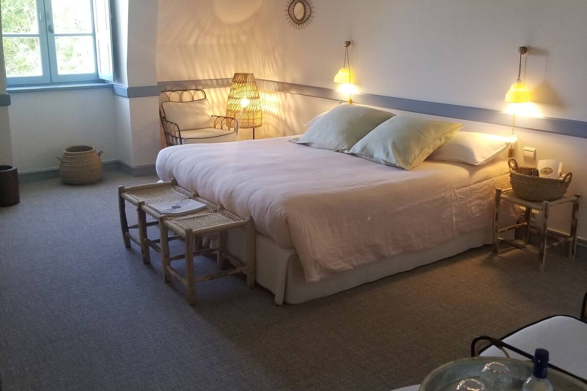 A bedroom with a bed, bedside lamps, a small table, and a window.