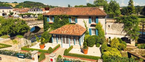 A historic building with a tiled roof, surrounded by well-maintained gardens and a small pond.