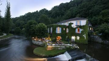 A riverside hotel with a waterfall, lush greenery, and a well-lit outdoor seating area.