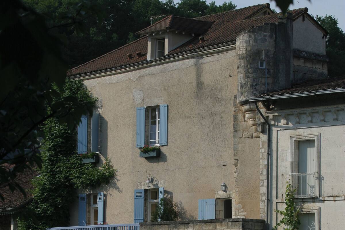 A historic building with stone walls, blue shutters, and a balcony with plants.