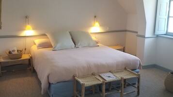 A bedroom with a large bed, two bedside lamps, a small table, and a window with curtains.