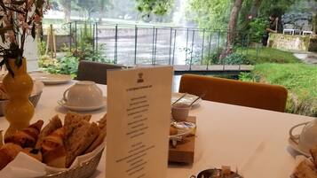 A table set for breakfast with a menu, bread, pastries, and a view of a river and greenery.