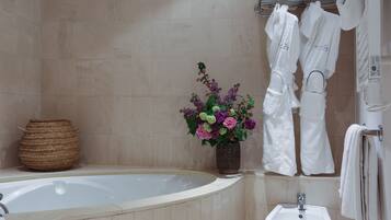 A bathroom with a bathtub, a sink, a woven basket, and a vase of flowers.