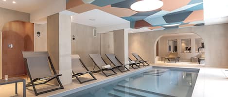 Una piscina interior moderna con sillones de descanso y un diseño de techo geométrico.