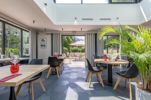 Un comedor moderno con suelo de patrón hexagonal, mesas de madera, sillas negras y plantas en macetas.