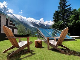 Two wooden Adirondack chairs facing a glass conservatory with a mountain view.