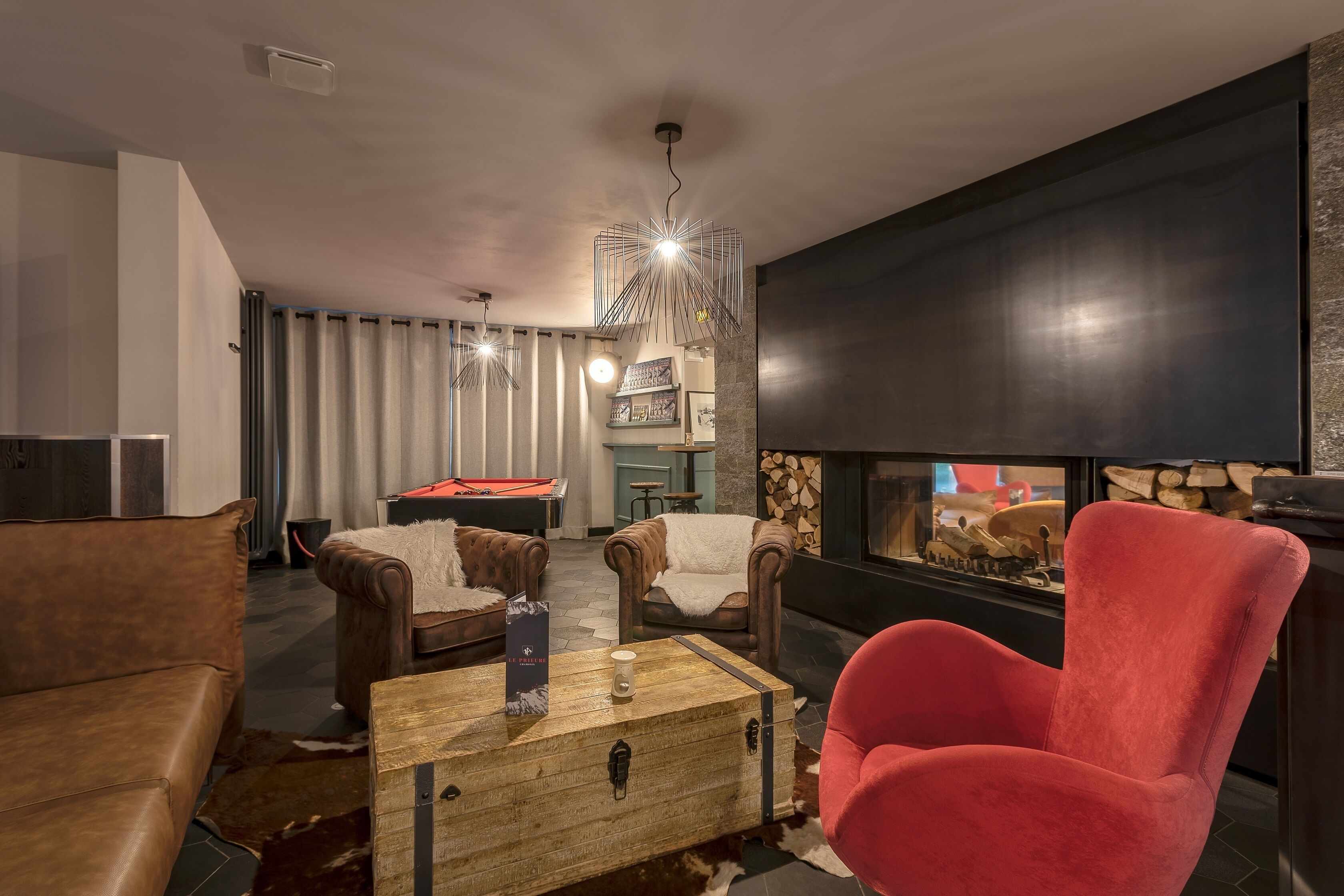 A modern living room with leather sofas, a wooden coffee table, and a red armchair. A pool table and a fireplace are also visible.