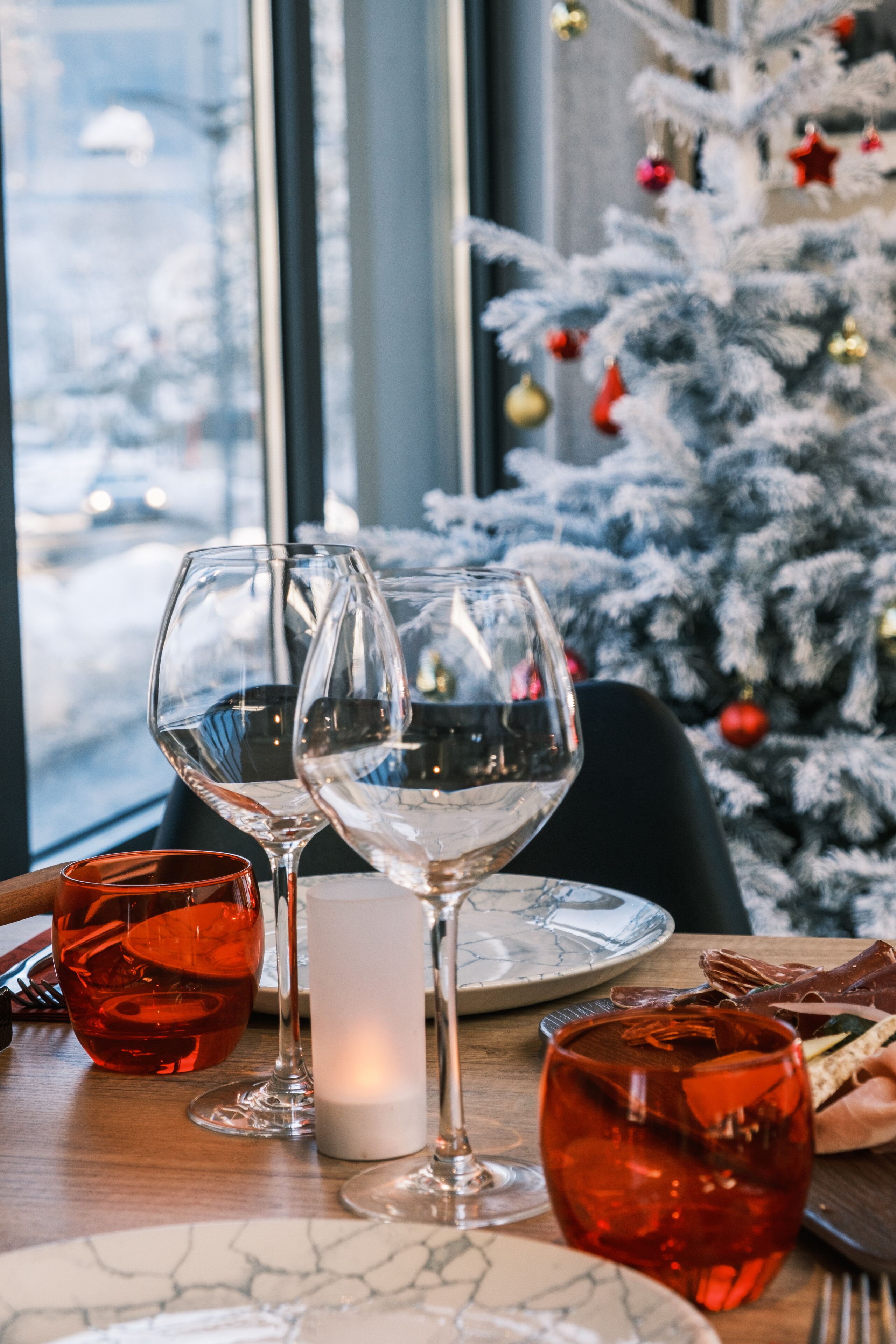 A dining table with wine glasses, a candle, and a Christmas tree in the background.