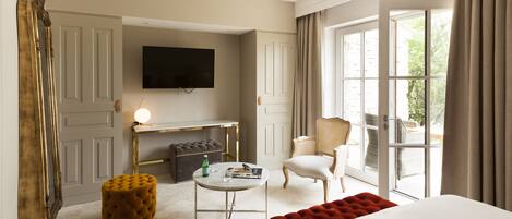 A hotel room with a bed, a television, a seating area with a table and chairs, and a view through a large window.