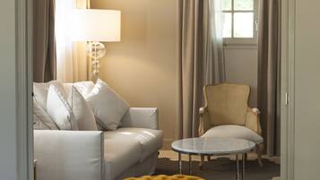 Une pièce comprenant un canapé, un fauteuil, un pouf, une lampe et des rideaux.
