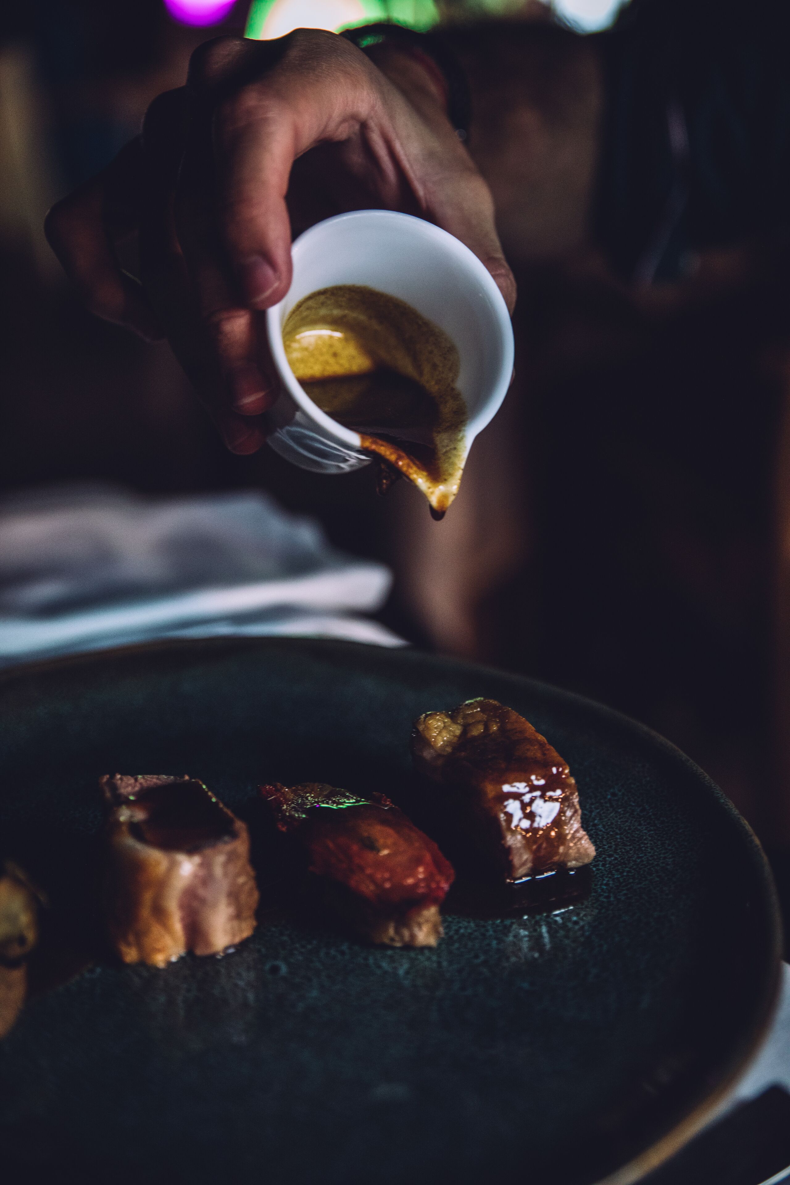 A hand pouring a liquid onto a plate with food items.