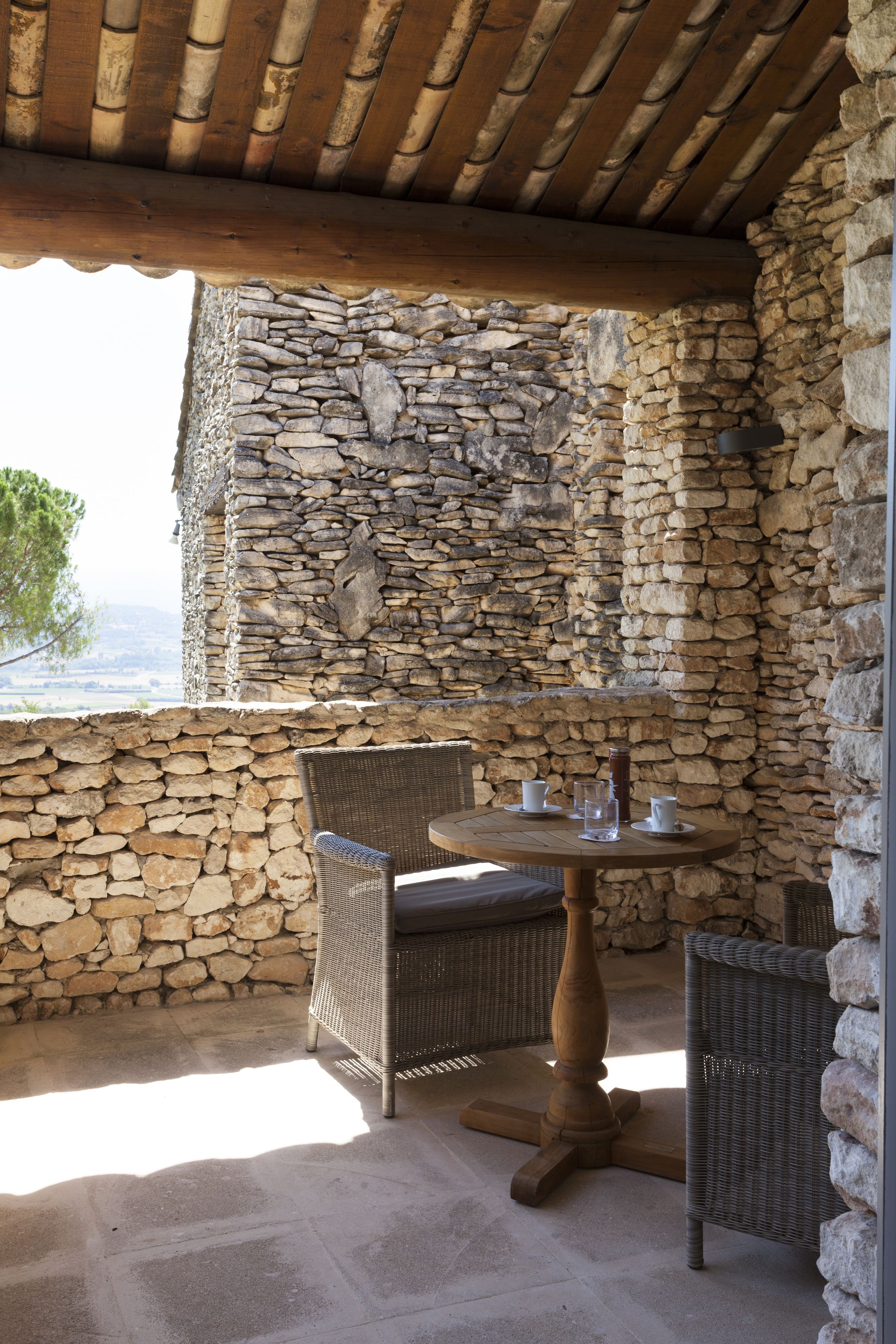 A stone-walled patio with wicker furniture and a table set for two.