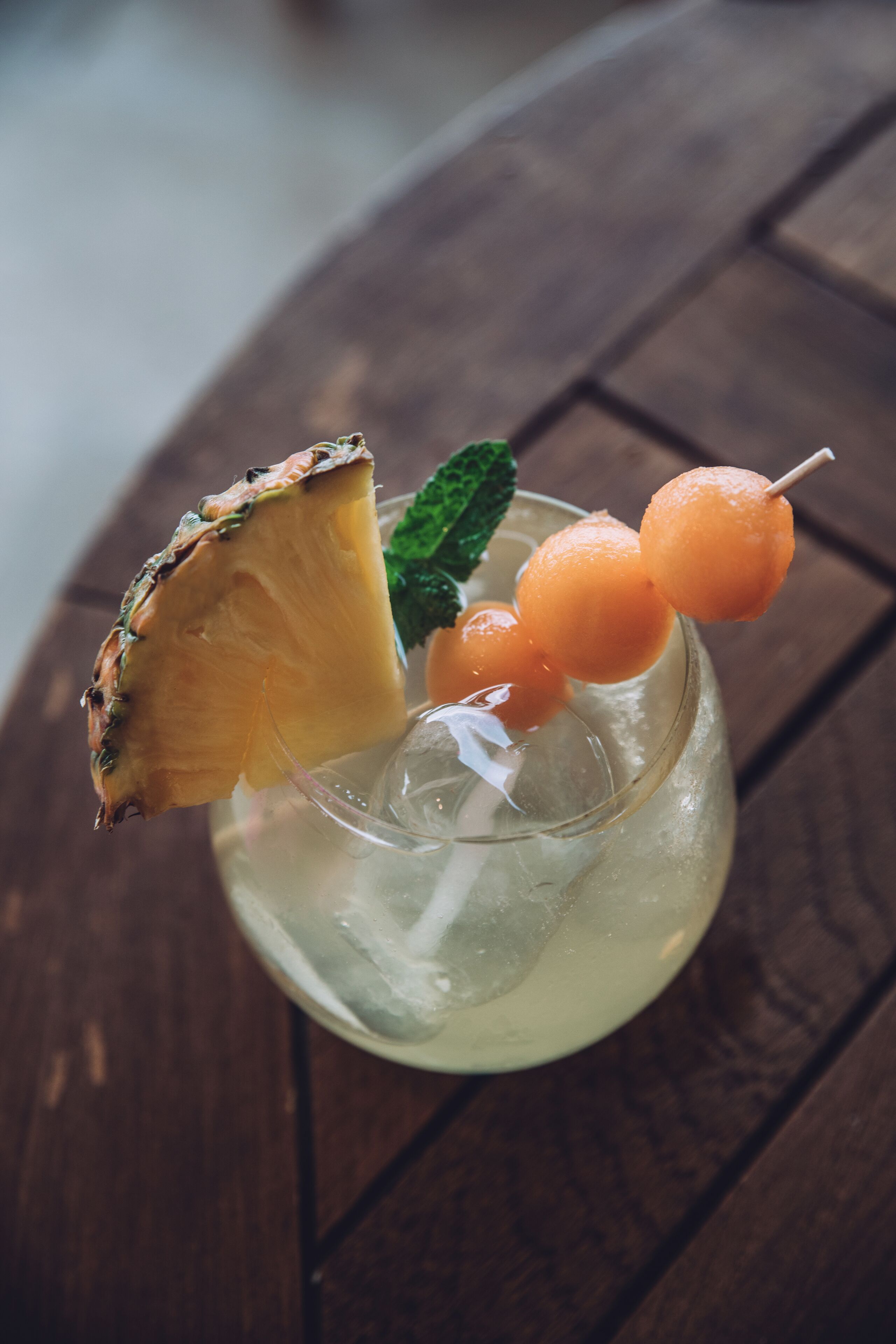 Un verre contenant une tranche d’ananas et des billes d’orange, posé sur une surface en bois.