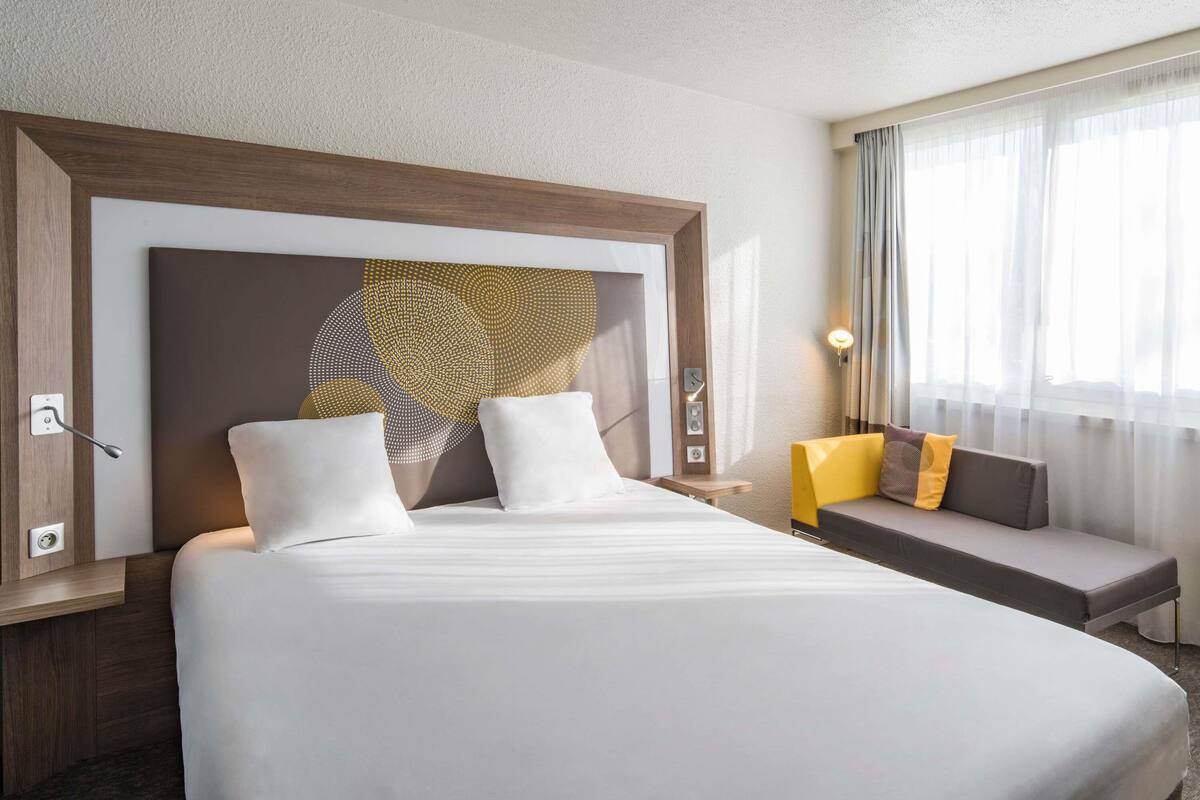 Une chambre d’hôtel avec un grand lit, un canapé, une œuvre d’art murale et une fenêtre avec des rideaux.