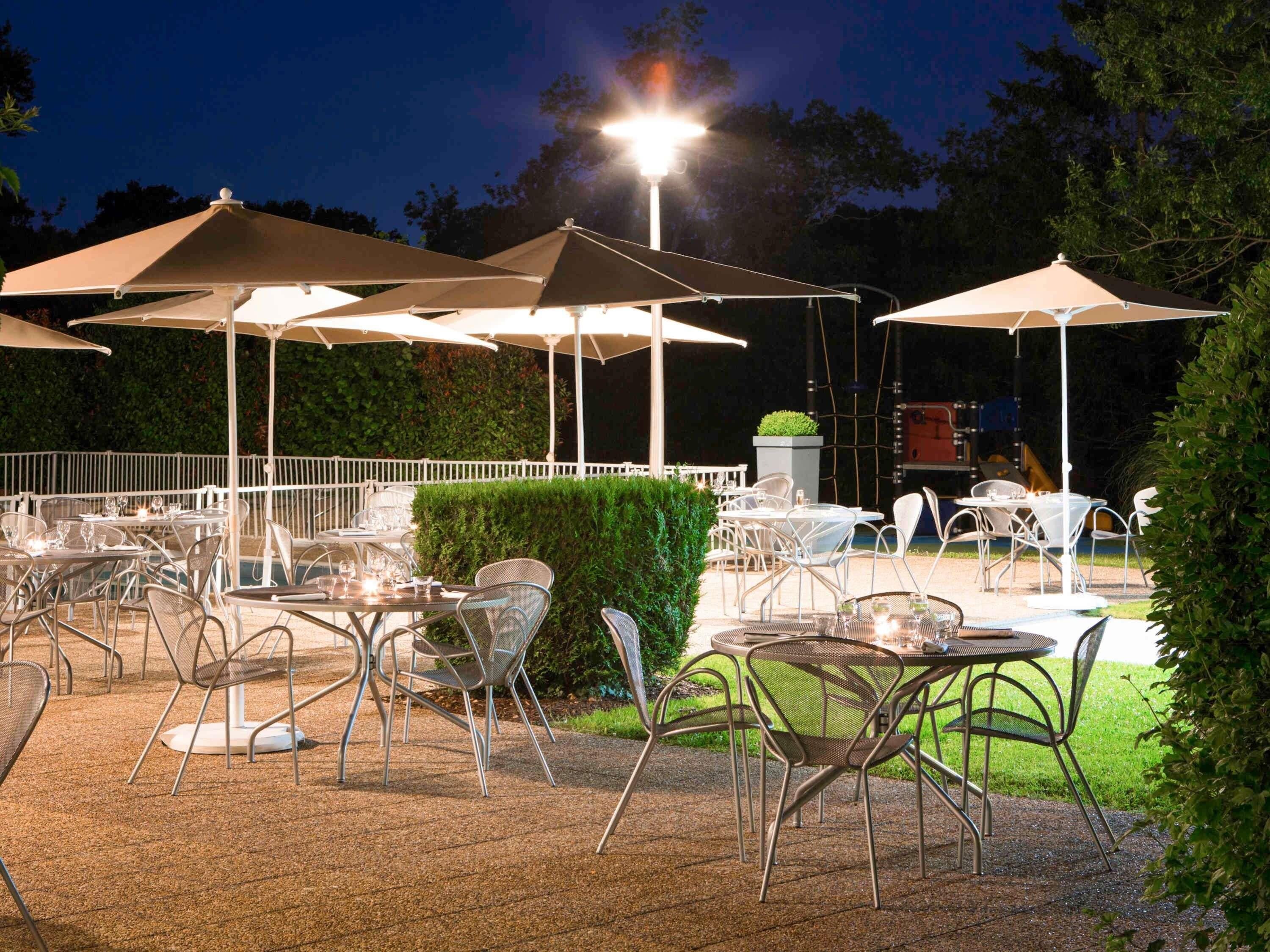An outdoor dining area with tables and chairs, umbrellas, and a well-lit environment.