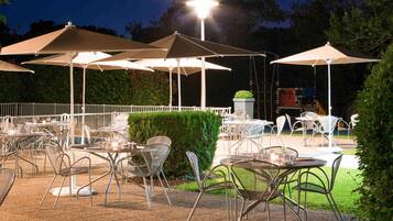 Un espacio de comedor al aire libre con mesas, sillas, sombrillas y un ambiente bien iluminado.