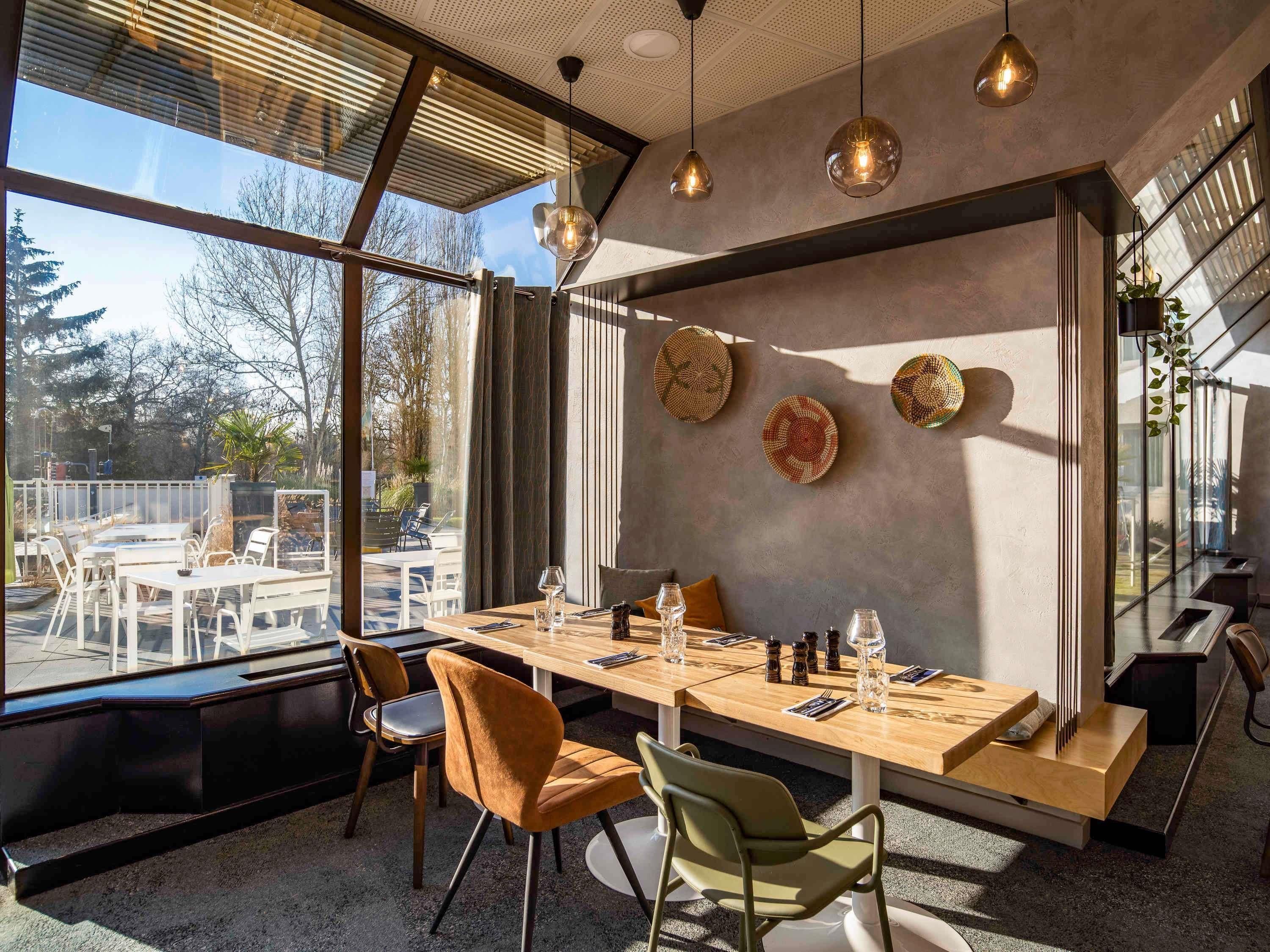 Un espace de salle à manger moderne, doté d’une grande table, de chaises et de luminaires suspendus.