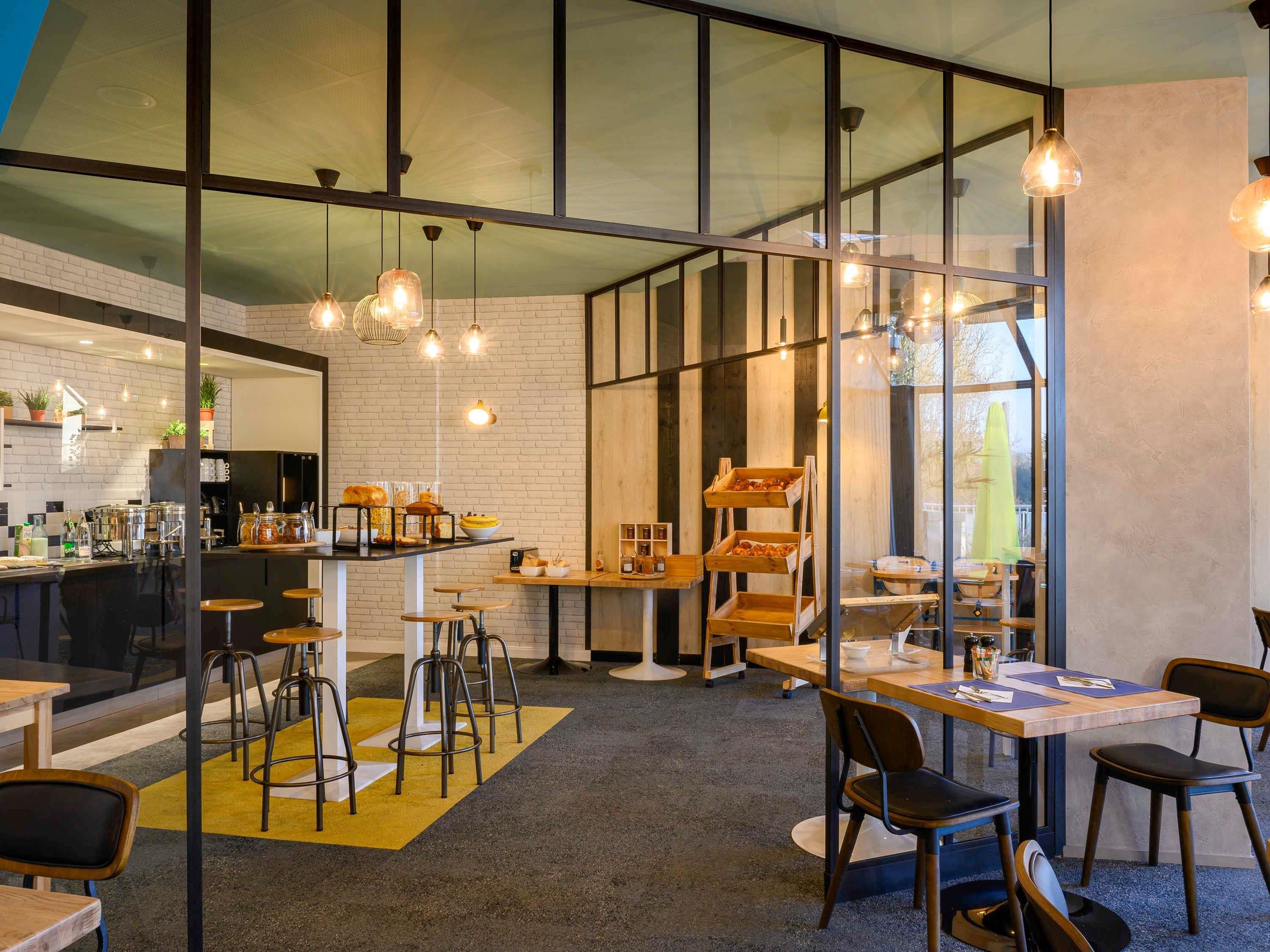 A modern cafe with a bar area, seating, and a glass wall offering a view.