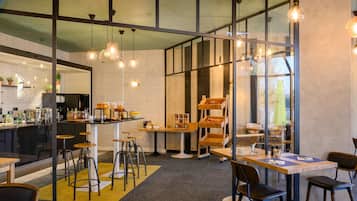 A modern cafe with a bar area, seating, and a glass wall offering a view.