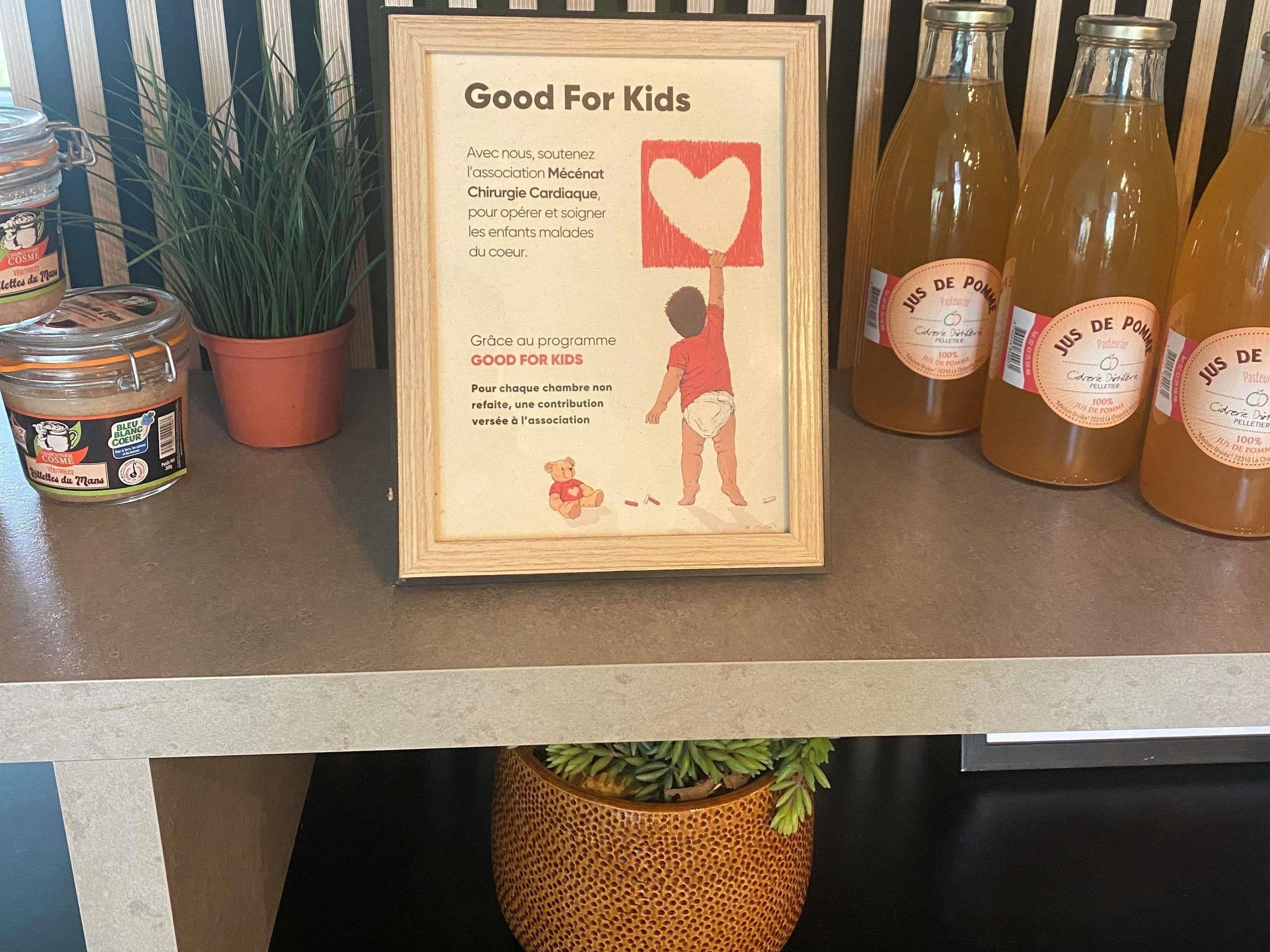 A framed sign with a child holding a heart, a jar of jelly, and bottles of juice on a counter.