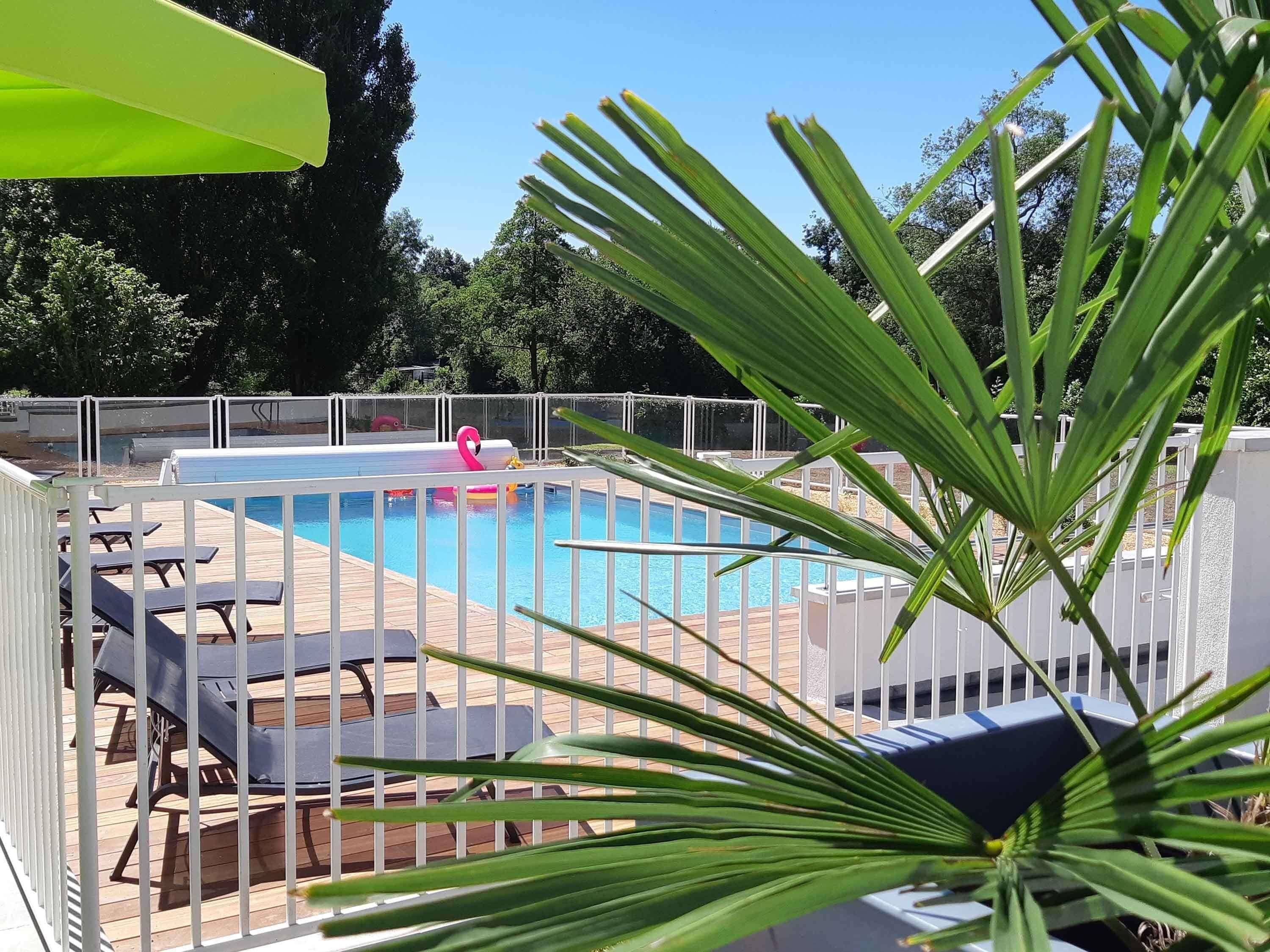 Une piscine agrémentée d’un flotteur en forme de flamant rose, entourée de mobilier blanc disposé au bord de la piscine et d’une terrasse en bois.