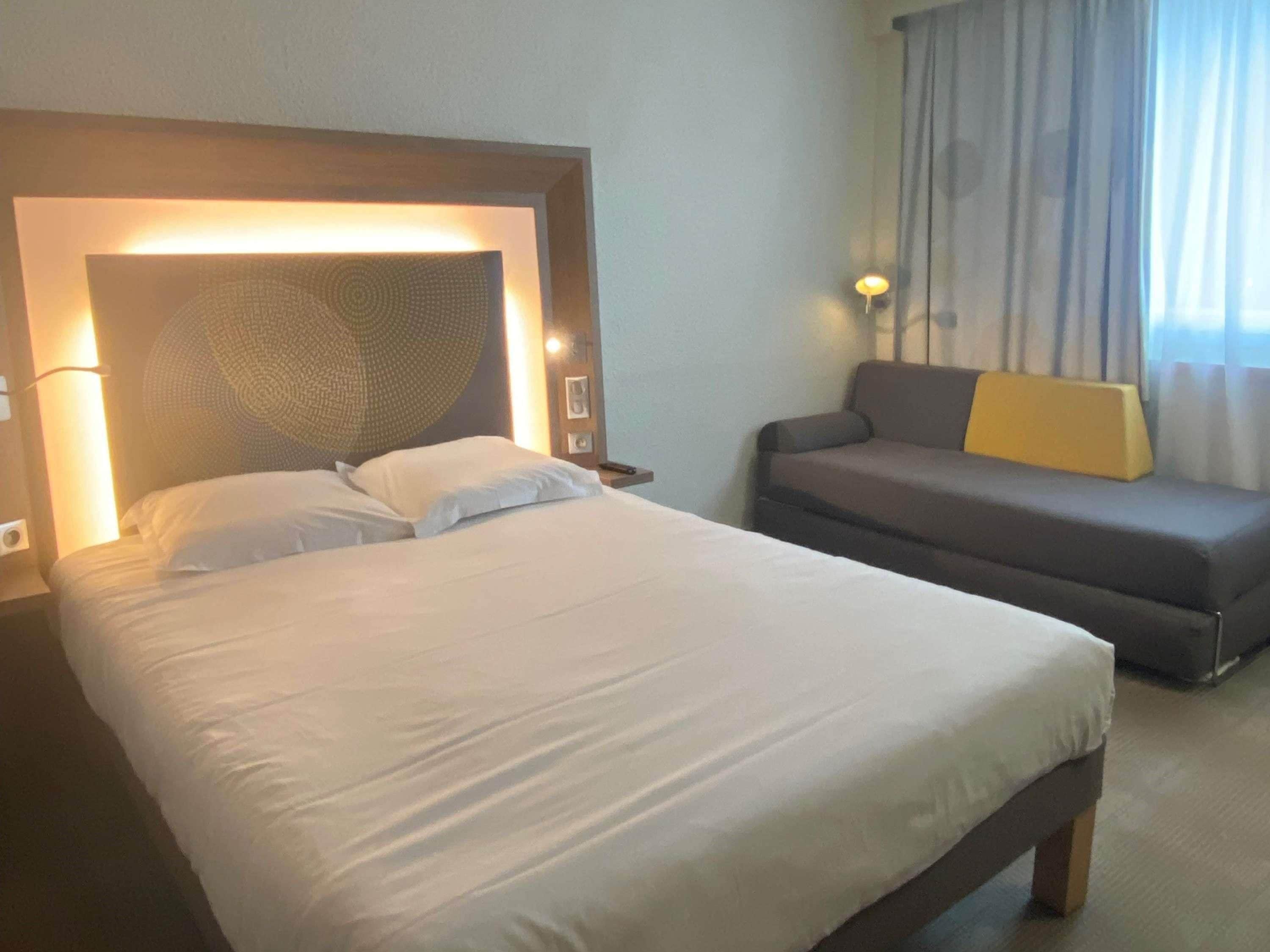 Habitación de hotel con una cama grande, un sofá y un cabecero de diseño texturizado.