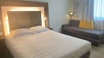 A hotel room with a large bed, a sofa, and a headboard with a textured design.