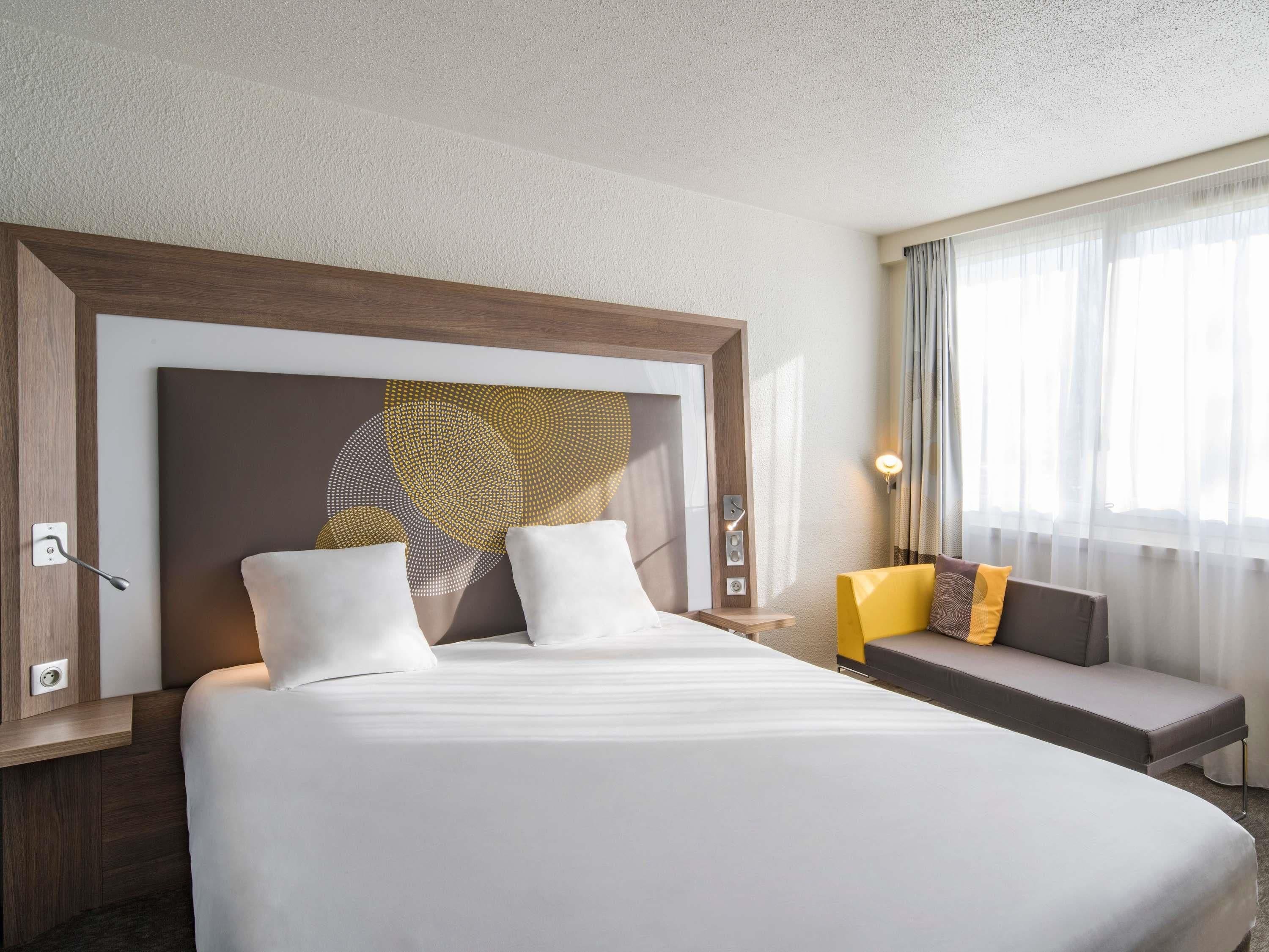 A hotel room with a large bed, a sofa, a wall art piece, and a window with curtains.