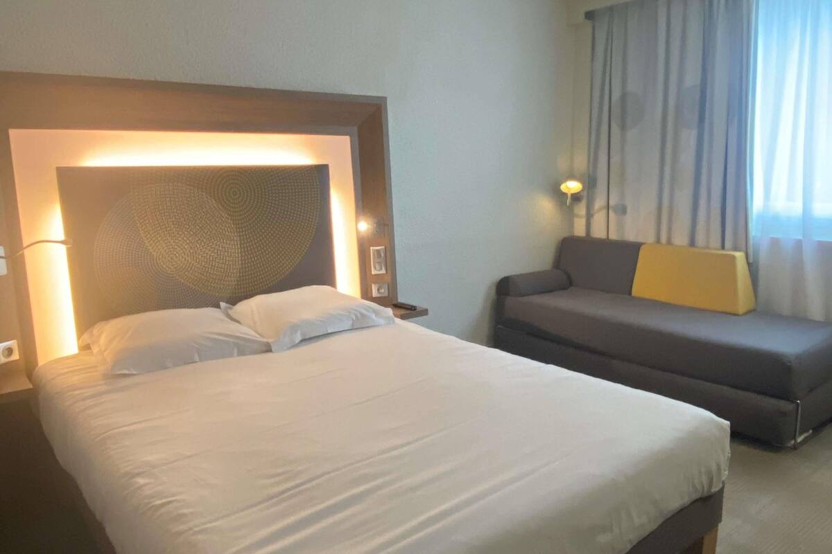 A hotel room with a large bed, a sofa, and a headboard with a textured design.