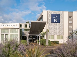 Un bâtiment moderne arborant un grand logo en forme de « N » sur sa façade, une entrée couverte et une enseigne indiquant « LA CHICANE BRASSERIE MAISON ».