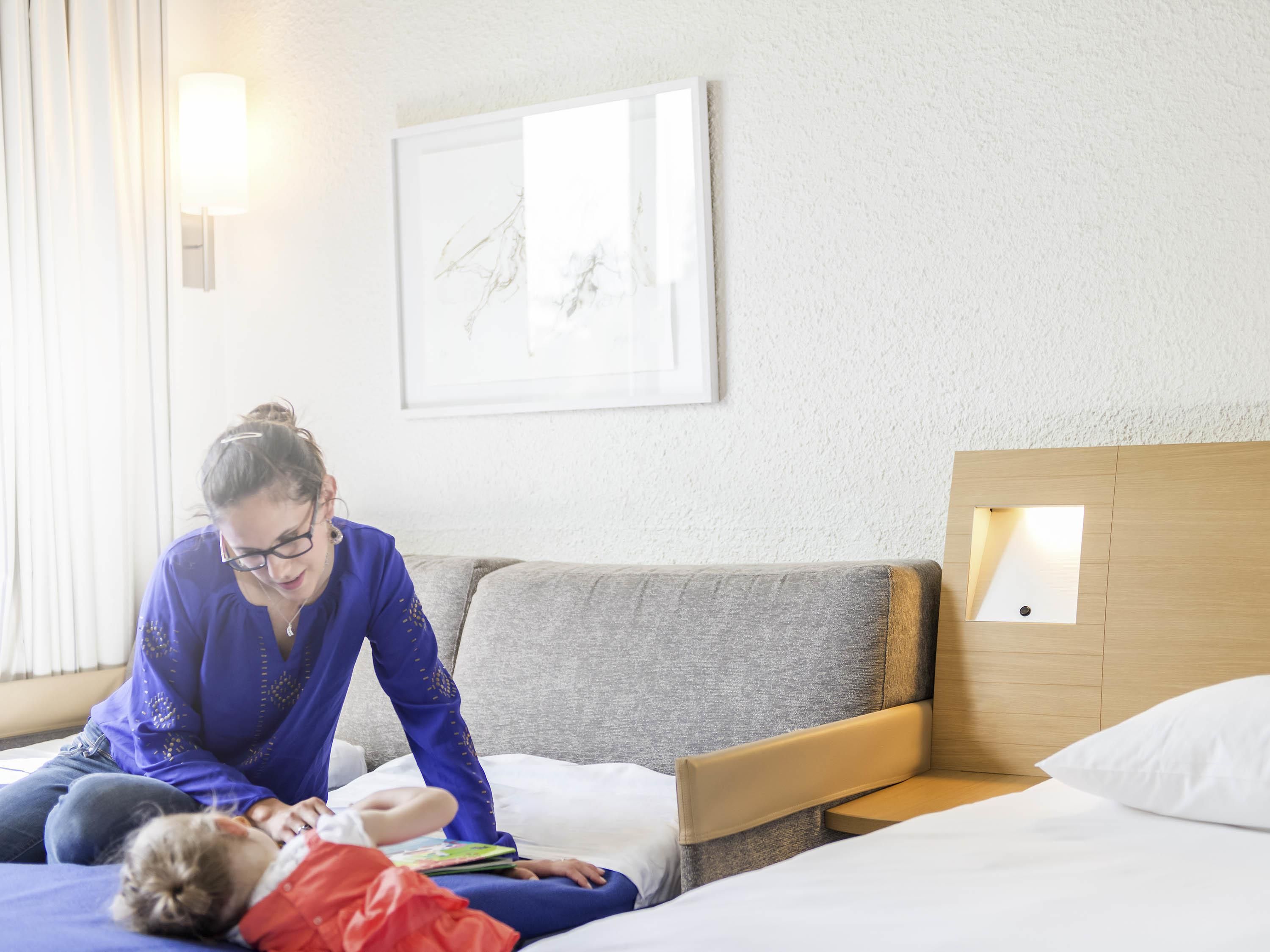 Hotellihuone, jossa on sänky, sohva, seinään kiinnitetty valaisin ja kehystetty taulu.
