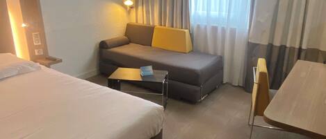 Una habitación de hotel con una cama, un sofá, una mesita y una silla.