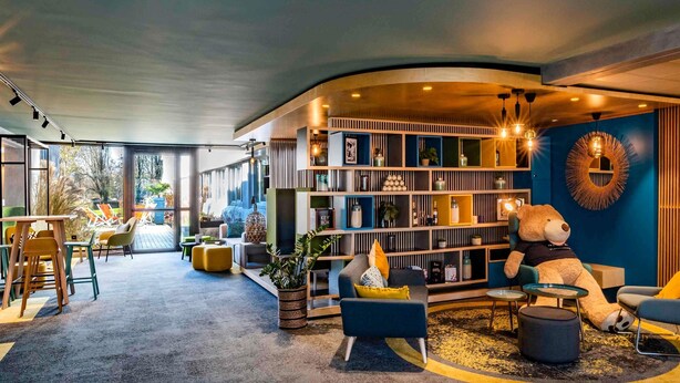 A modern interior with a curved seating area, a bookshelf, and a large teddy bear.