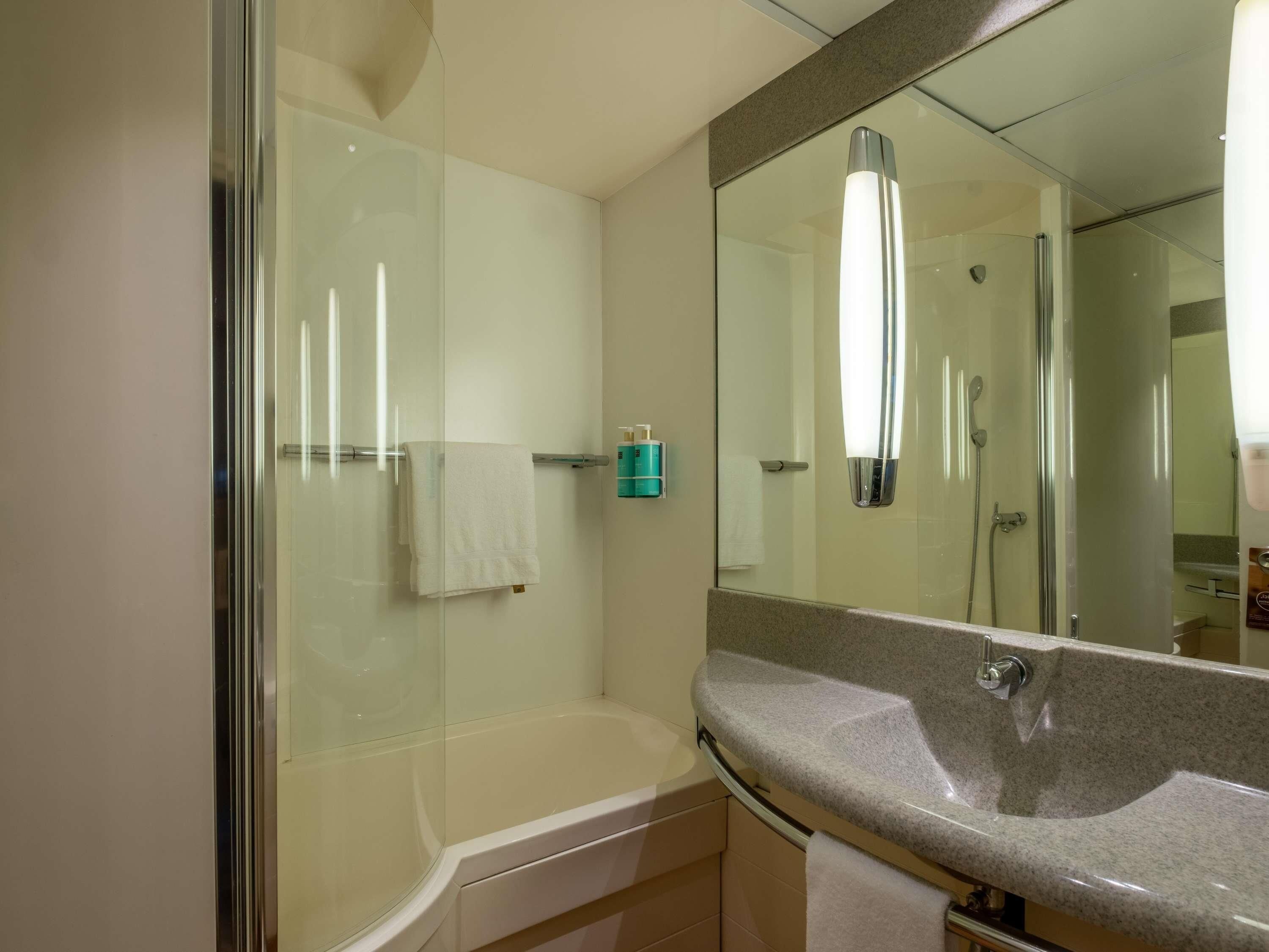 A modern bathroom with a glass-enclosed shower, a white bathtub, and a granite countertop sink.