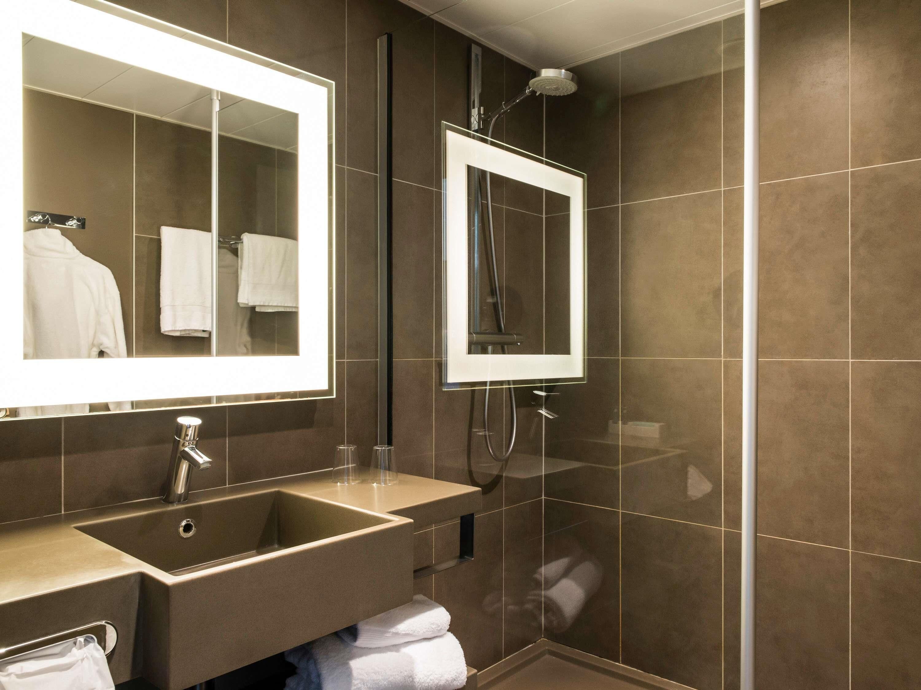 A modern bathroom with a large mirror, a sink, and a shower.