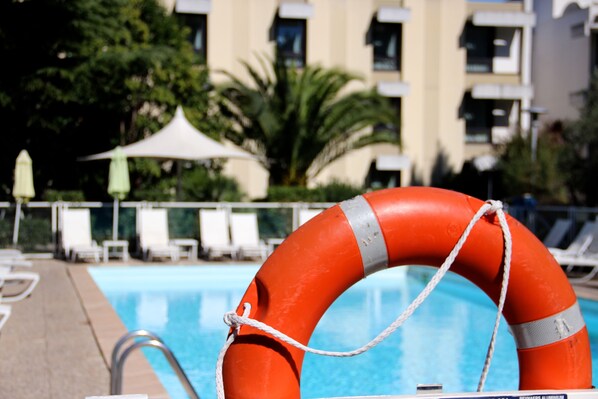 A lifebuoy by a poolside with lounge chairs and a palm tree in the background.