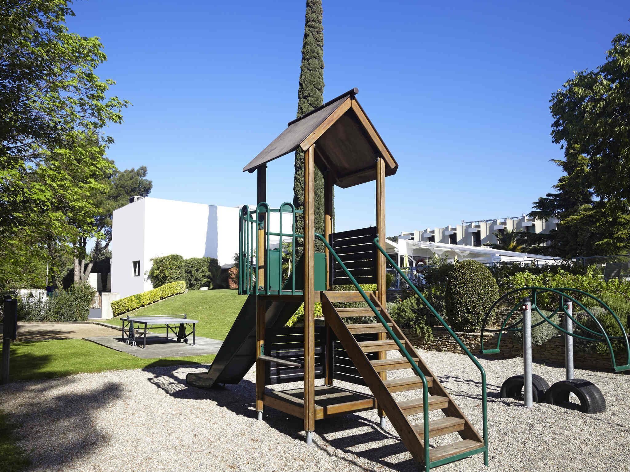 Ein Spielplatz mit einer Holzrutsche und Treppen, umgeben von Kies und Pflanzen.