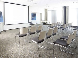 Un salón de conferencias con pantalla de proyector, filas de sillas, una mesa con una computadora portátil y un cartel que dice 'BIENVENUE Welcome'.