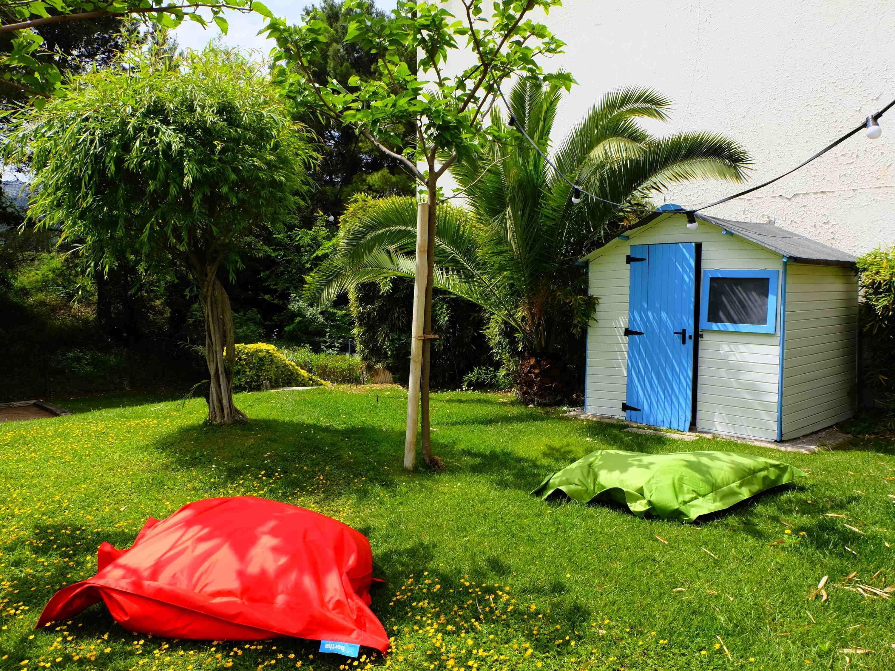 A small shed with a blue door and window, surrounded by lush greenery and a grassy lawn.