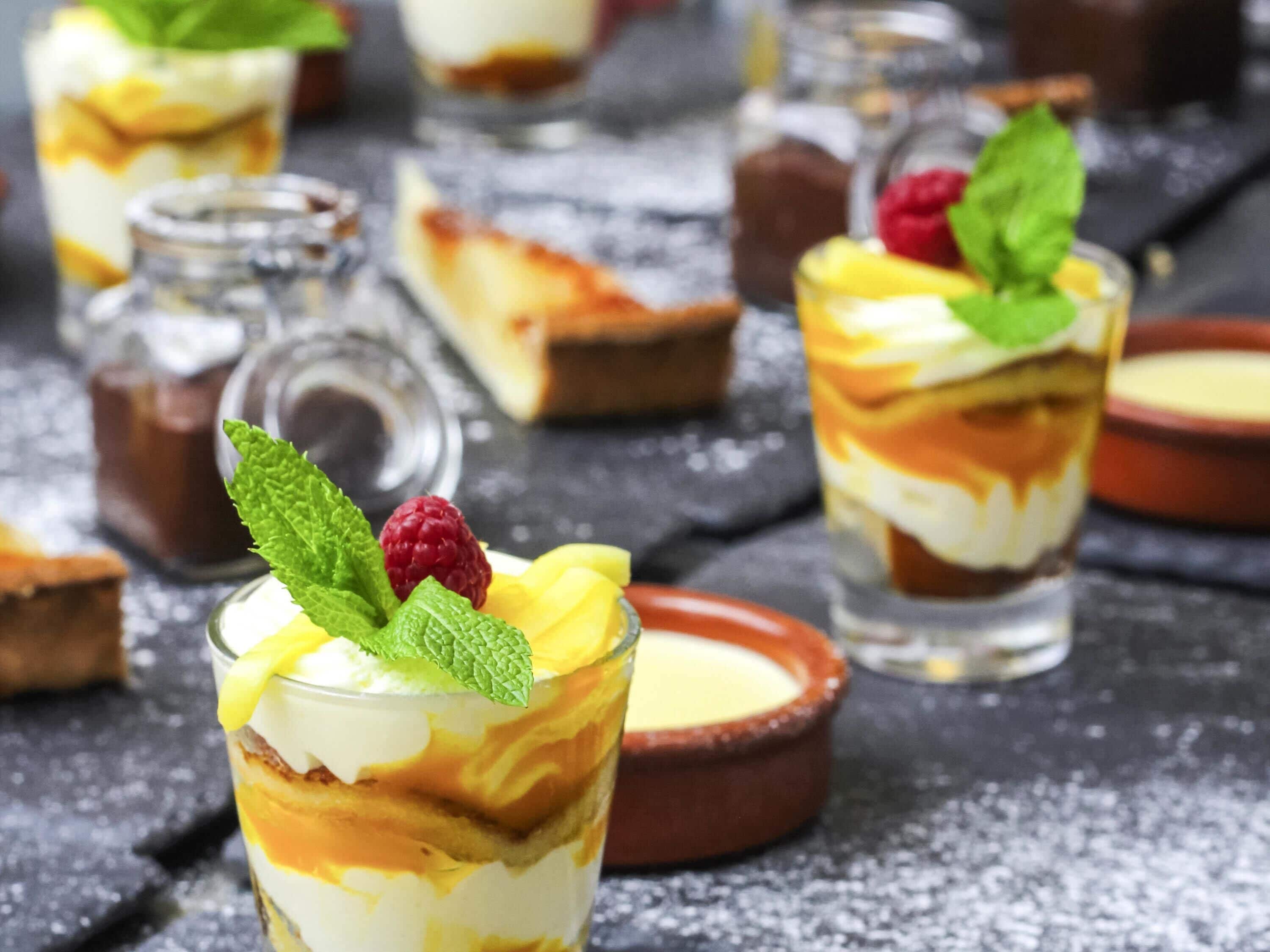 Presentación de postres con parfait en capas, decorado con hojas de menta y frambuesas, sobre una superficie texturizada.