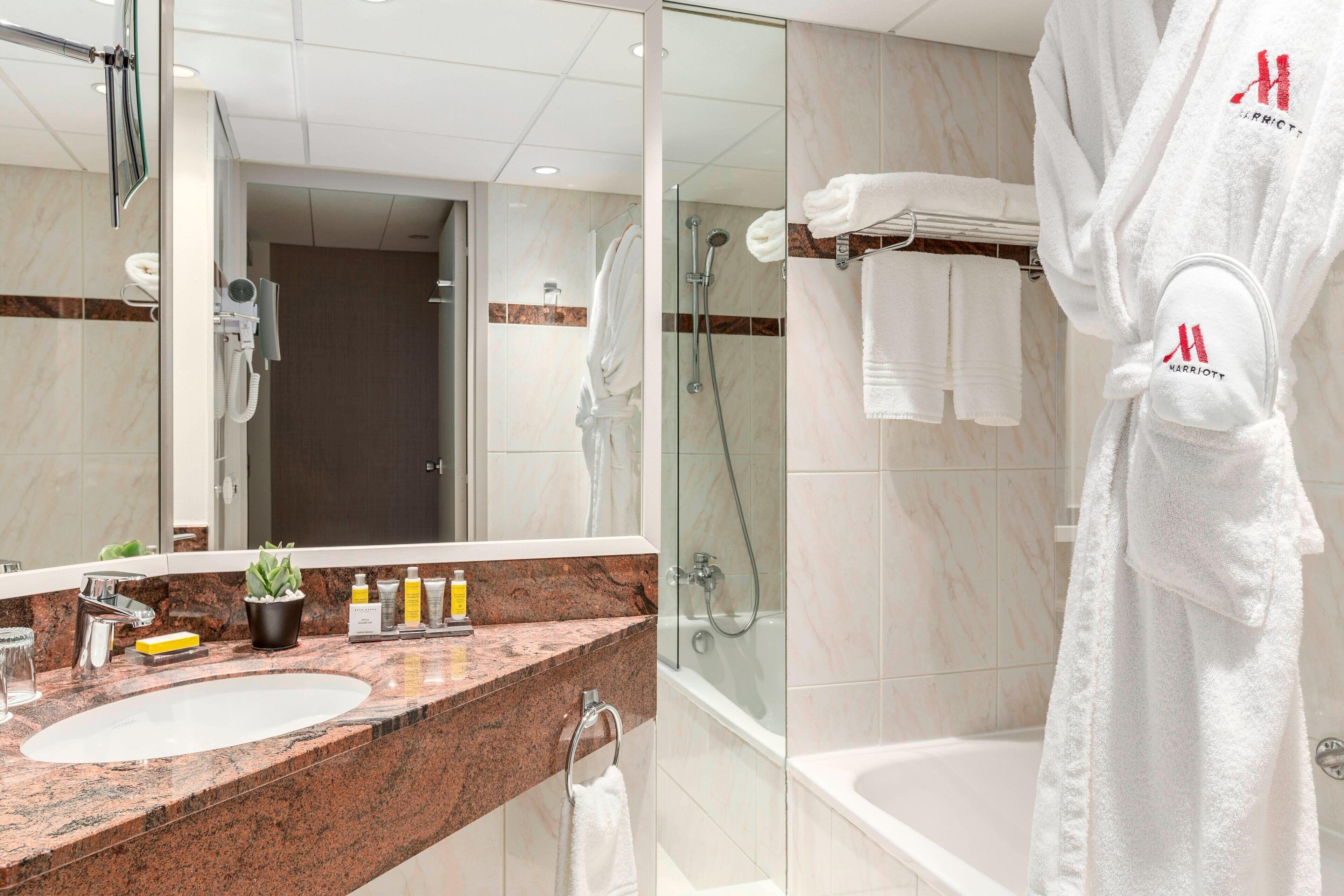 A bathroom with a marble sink, a glass shower enclosure, and a white bathrobe hanging on a rack.