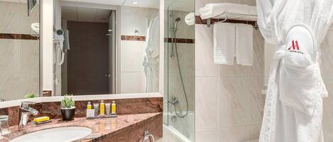 A bathroom with a marble sink, a glass shower enclosure, and a white bathrobe hanging on a rack.
