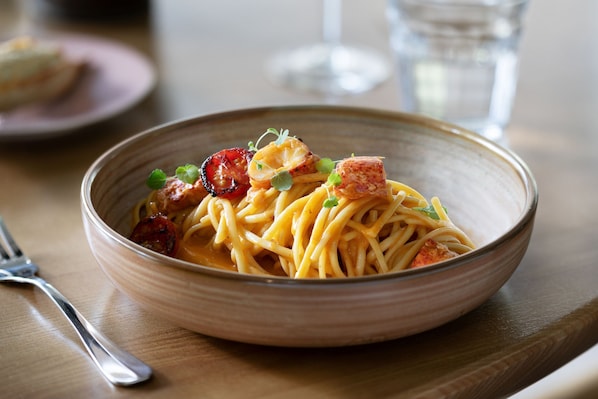 A bowl of pasta with cherry tomatoes and green onions on a wooden table.