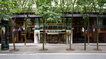 A Marriott hotel entrance with a glass facade, trees, and flags.