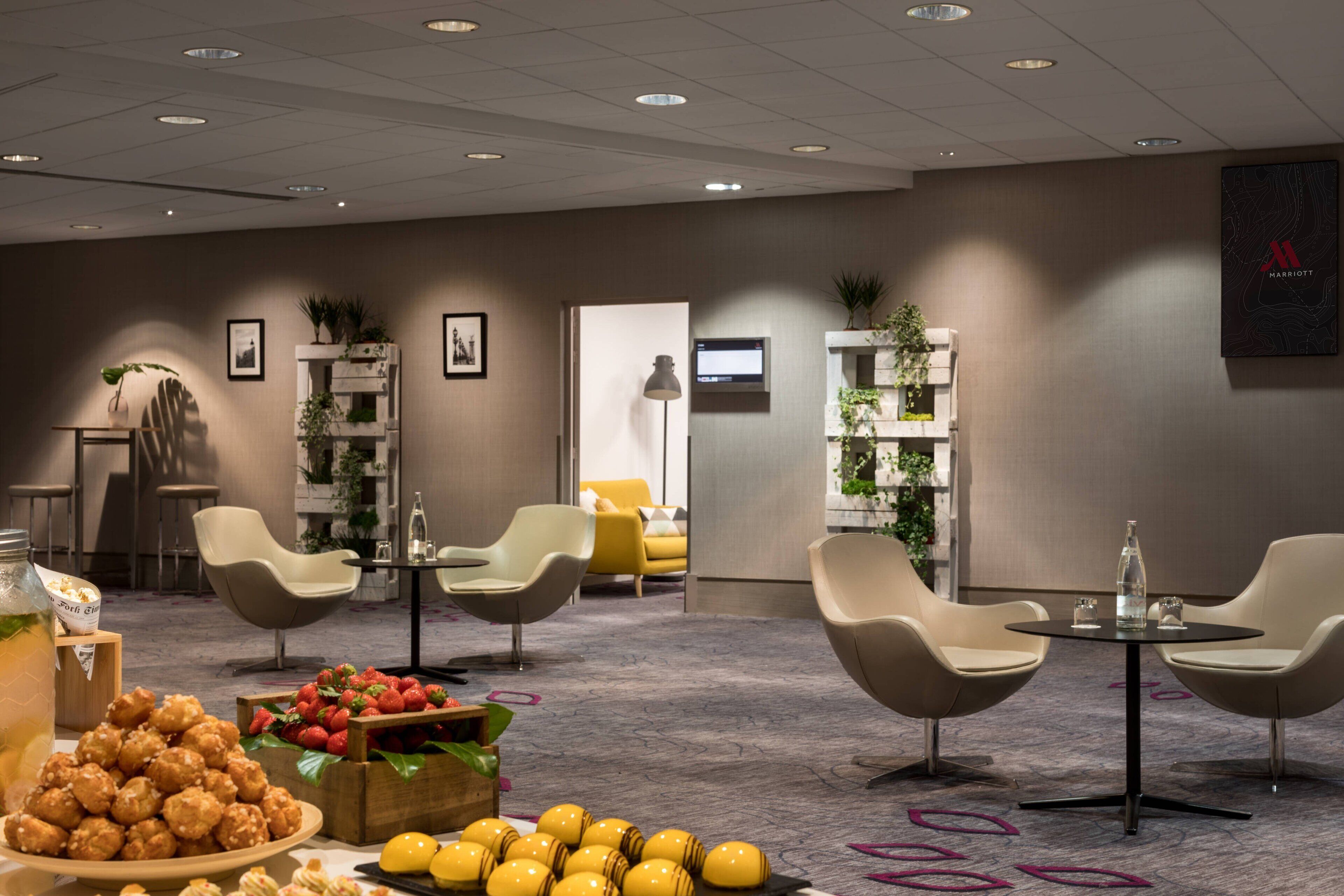 A modern hotel lobby with seating areas, a reception desk, and a buffet with food and drinks.