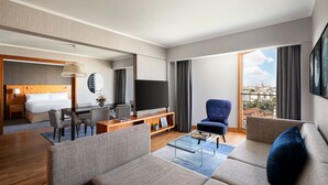 A modern hotel room with a living area, a dining space, a bedroom, and a large window offering a city view. - Paris Marriott Rive Gauche Hotel & Conference Center (Paris)