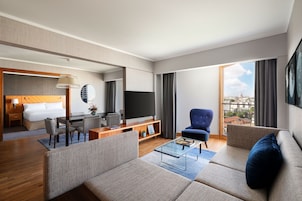 Una habitación de hotel moderna con sala de estar, comedor, dormitorio y un amplio ventanal con vistas a la ciudad.